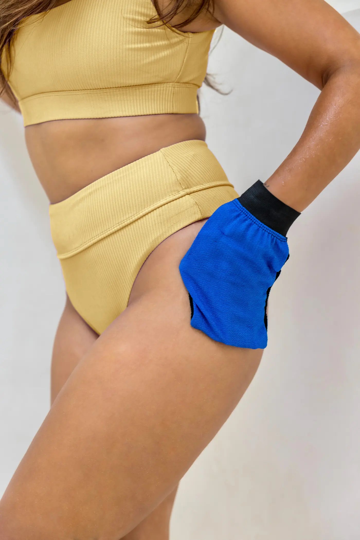 Model using Naked Tan blue exfoliating mitt to remove residual self-tan and prepare skin for reapplication